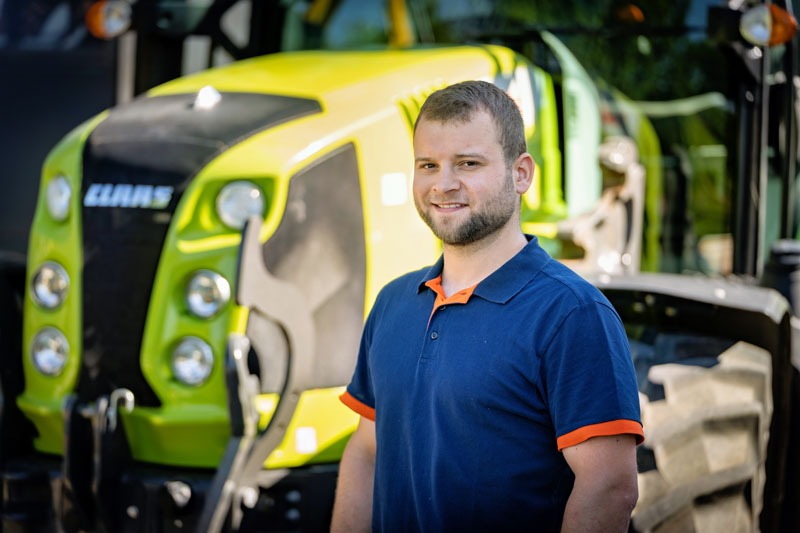Portrait des Inhabers Martin Strobel in einem blauen Polo-Shirt, vor einem leicht verschwommenen, grünen Traktor